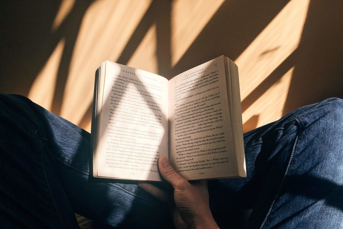 person holding book sitting on brown surface